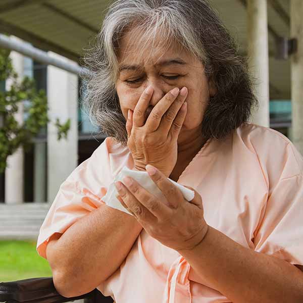 Older lady hand over her mouth coughing with tissue in the other hand.