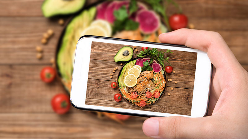 hand taking cell phone picture of healthy fats in salad