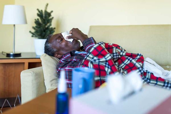 Man blowing his nose laying on couch