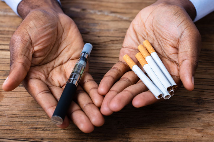 man holding a vape pen and cigarettes