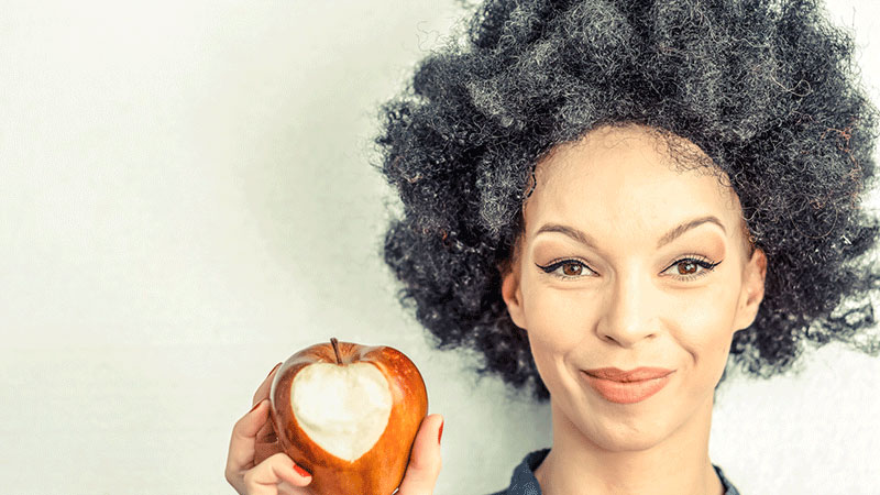 gray-haired woman eating apple with heart shape bite