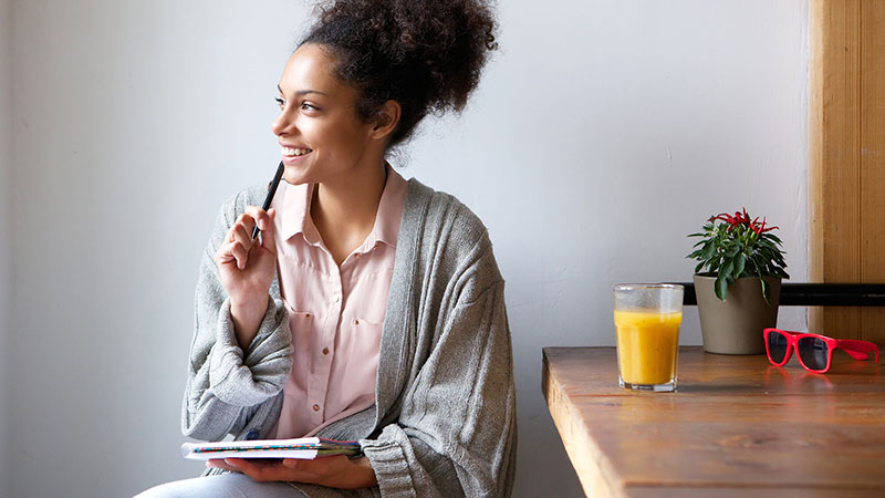 smiling African American woman writing in journal in pajamas