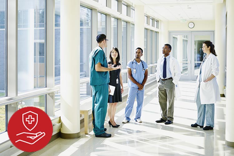 Medical team standing in hospital hallway next to windows. AHA QCOR meeting icon in lower left corner.