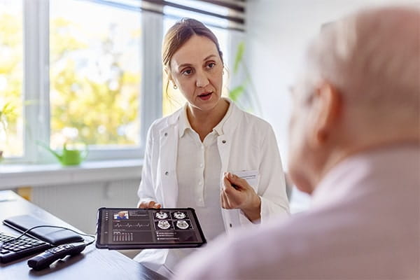Doctor using a digital tablet to discuss a brain scan with a senior patient in clinic