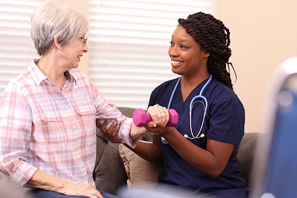 An older female stroke patient practices physical therapy with a smiling health care therapist.