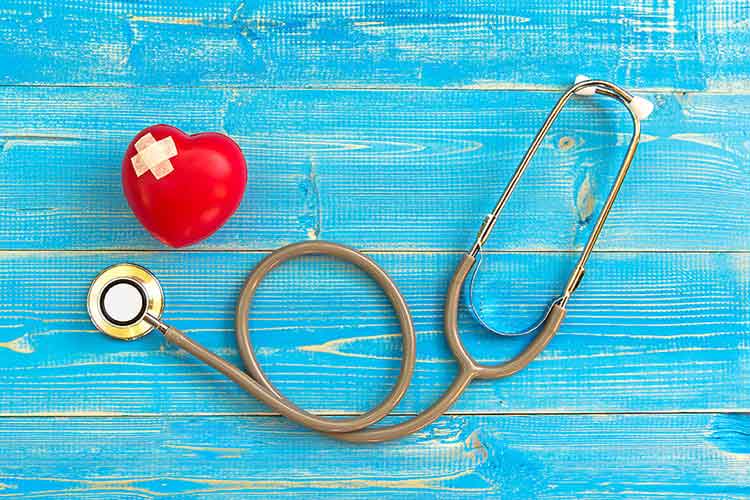 A plastic heart with band-aids sitting on a blue wood table next to a doctor's stethoscope.