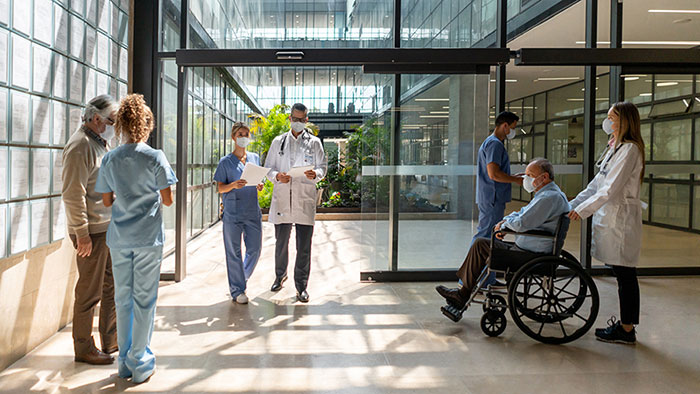 Doctors, nurses, and a patient in a wheelchair, passing through a sunlit atrium