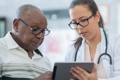 Female doctor consulting senior male patient both looking at ipad