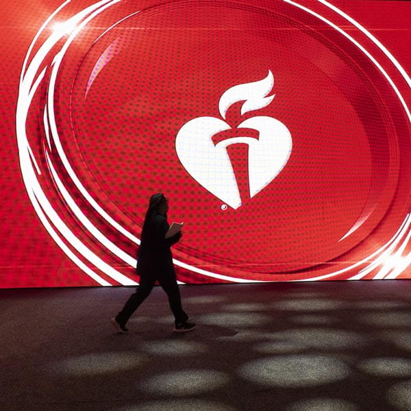 An AHA Scientific Sessions attendee walks past the American Heart Association logo on an electronic wall.