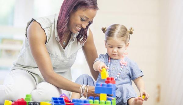 A young smiles as she plays colored blocks with a little girl.