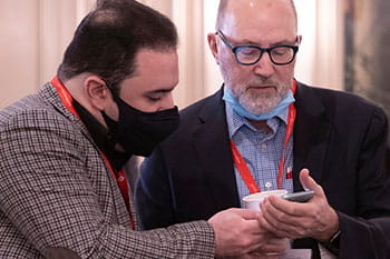 Two men looking at a mobile phone at an AHA conference. One is wearing a mask.