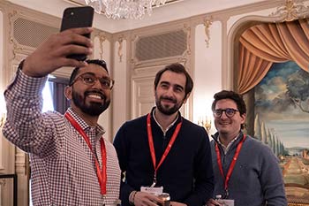 Three conference attendees smile for a mobile phone as one of them takes a selfie of the group.