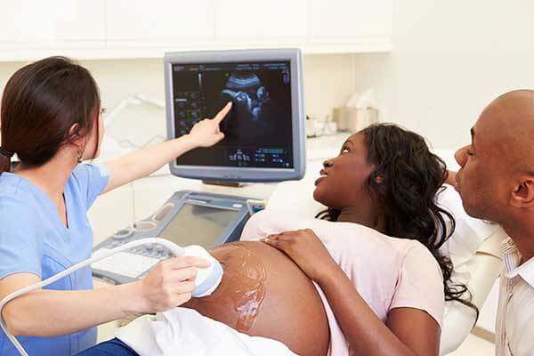 Pregnant woman and her partner look at ultrasound screen with technician