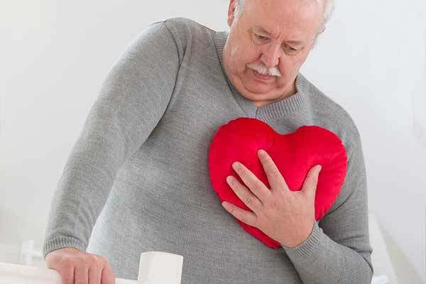 Older senior clutches heart-shaped pillow to his chest as if he has angina