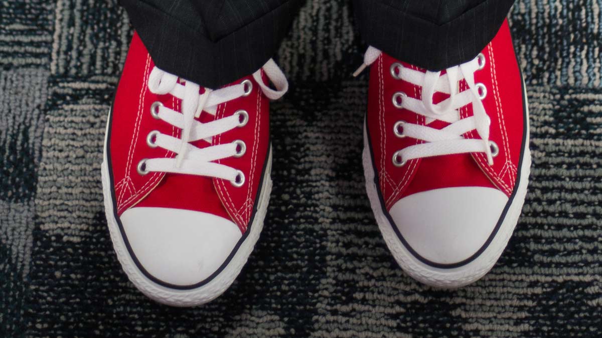 A photo of feet in red sneakers topped by dress slacks.