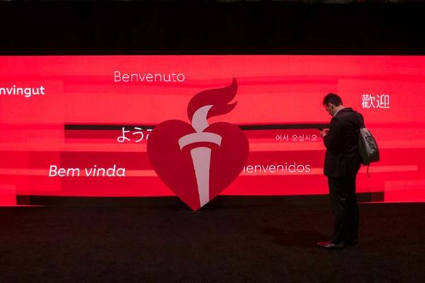 A Scientific Sessions attendee stands in front of an electronic billboard that reads "Welcome" in different languages