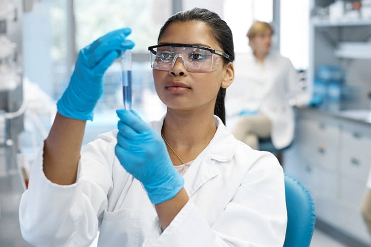 Young female scientist examining medical sample in test tube. Confident healthcare worker is working at research center. She is wearing lab coat.