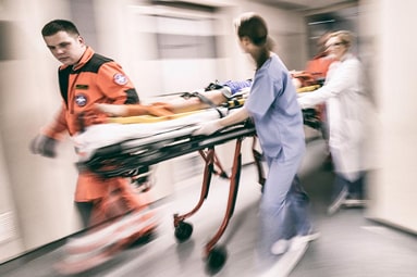 A male EMT and a female doctor rushing a patient on a gurney into the emergency department from the hospital's ambulance entrance.
