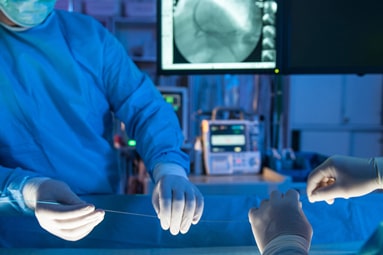 Two medical professionals dressed in blue surgical gowns perform a cardiac stent procedure in an operating room.