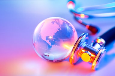 A close-up of a crystal globe next to stethoscope on a blue and pink background