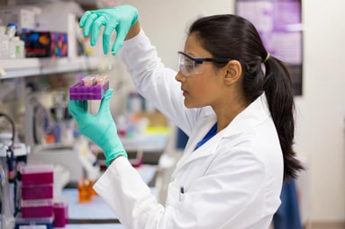 A young female researcher examining a tray of test tubes in the lab.