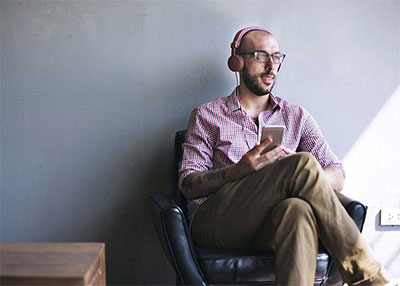 man with earbuds sitting down listening to phone