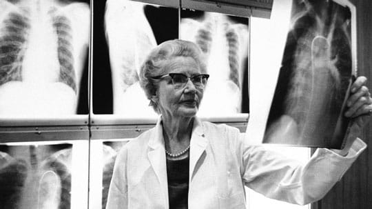 Black and white image of Helen Taussig with x-rays behind her and holding one up