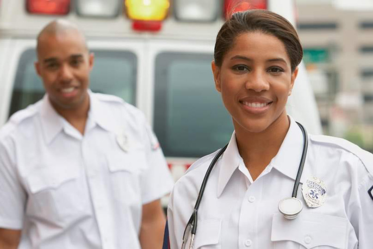 Male and female paramedics standing behind an ambulance and smiling