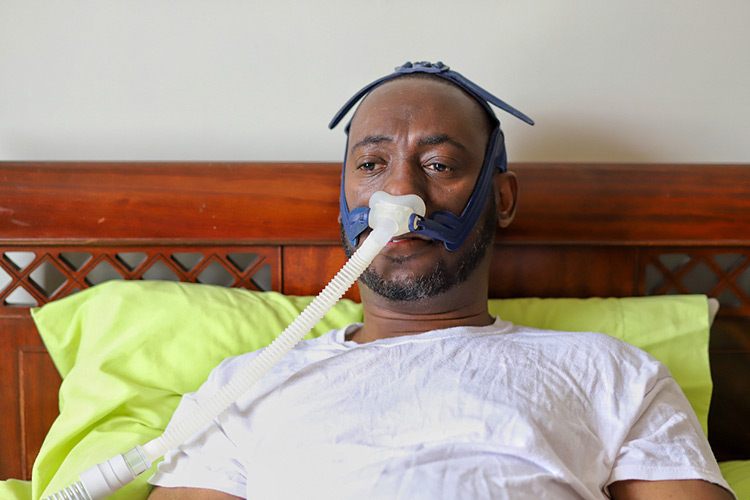 An African-American man wearing cpap mask while laying in bed.