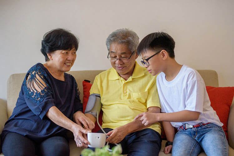 Senior Asian man measuring his blood pressure with the help of his wife and son.