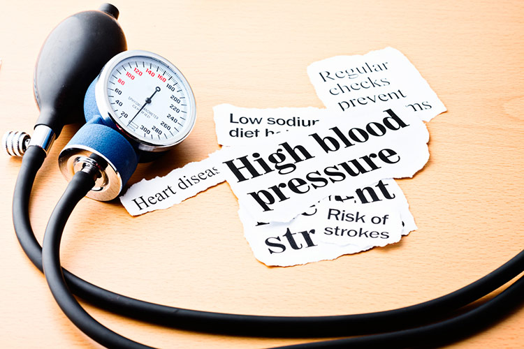 Headlines on high blood pressure, heart disease, and the risk of strokes on a wooden desk next to a blood-pressure gauge.
