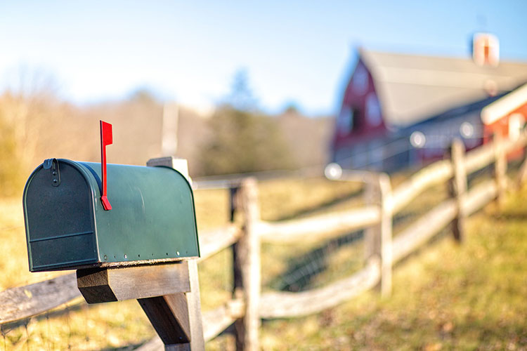 mailbox with raised flag outside along a rural wooden fence