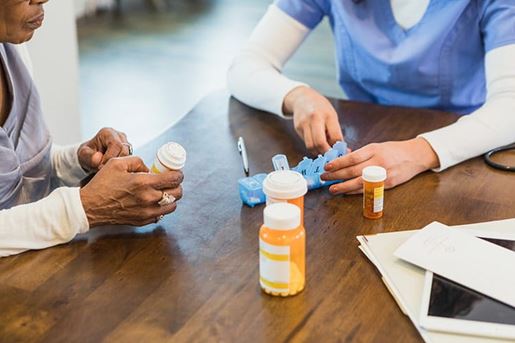 An unrecognizable female nurse shows an elderly patient how to organize her medication into a daily pill organize