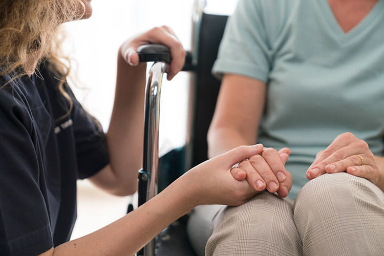 nurse holding hands of senior woman in wheelchair