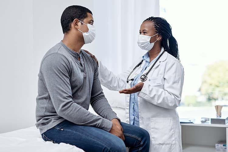 Black masked male patient and female doctor talking during an exam in the office