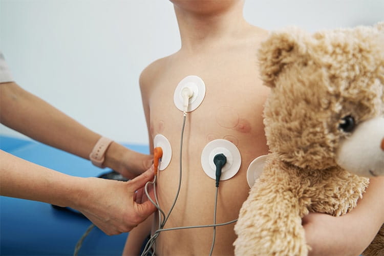 Close up of doctor attaching electrocardiograph sensors on boy chest while performing electrocardiogram test in clinic