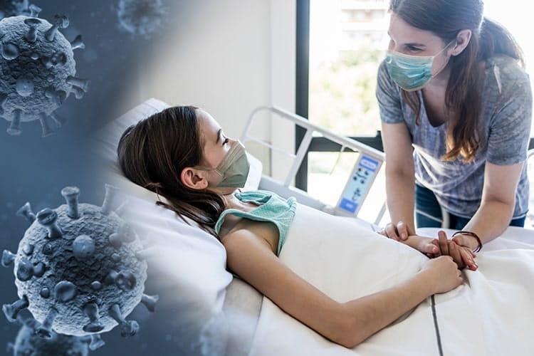 Loving mother holding her daughter’s hand while she is lying down on hospital bed both wearing protective face masks with a COVID virus superimposed
