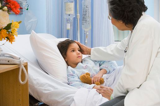 Senior female doctor checking on girl in hospital bed