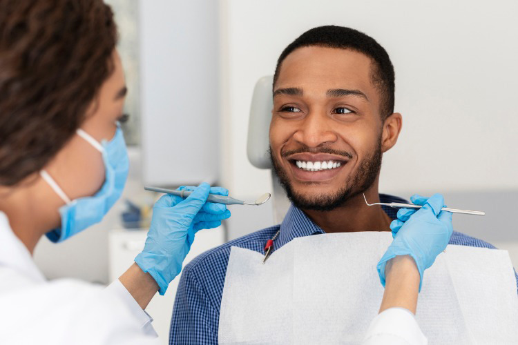 Close up of young black man in dentist chair smiling at his doctor.