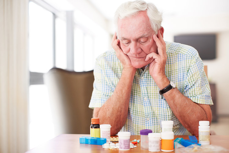 Senior man sitting and looking at his medication despondently.