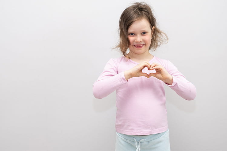 young girl smiles while making heart symbol with hands