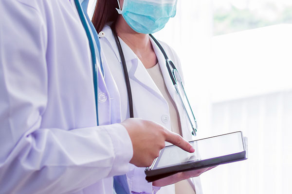 Two healthcare professionals in white coats looking at data on a digital tablet.