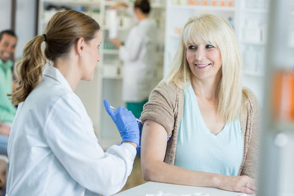 Pharmacist pushes needle into arm of smiling patient during flu shot