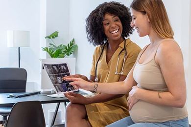 African American female doctor sits next to a pregnant patient reviewing ultrasound images