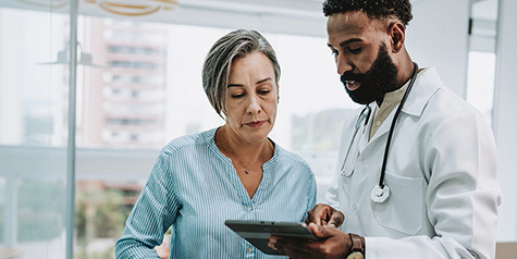 Male doctor showing information on the digital tablet he is holding to a female patient.