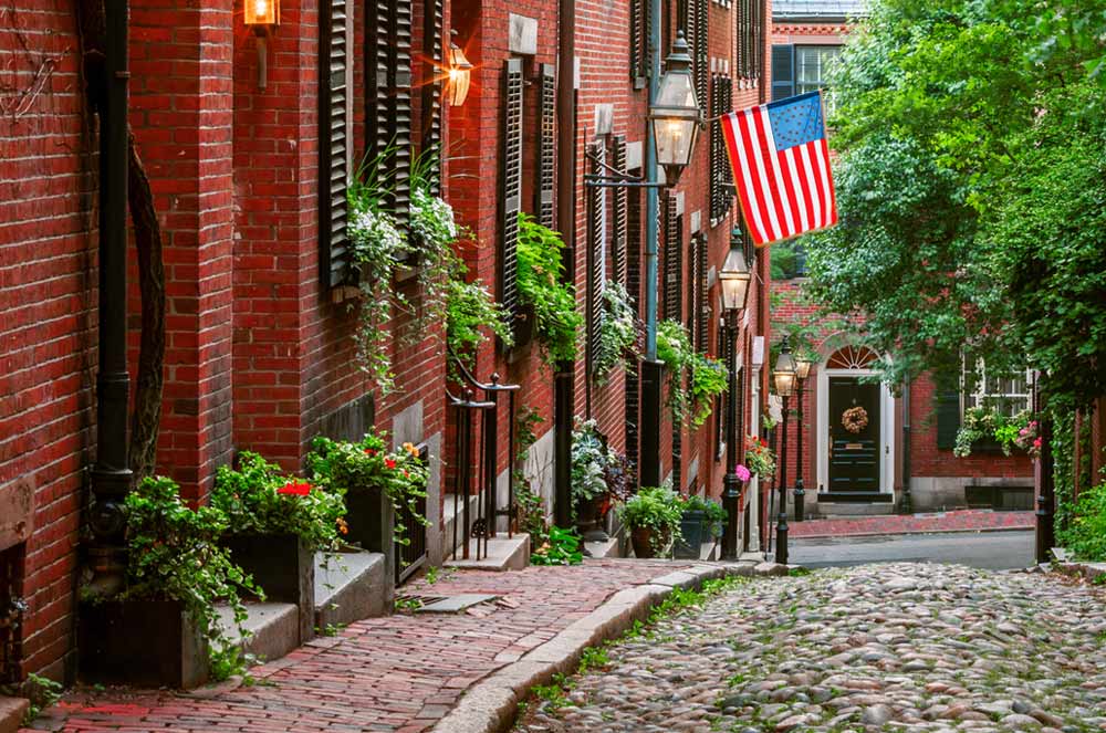 Brick townhomes and a cobble-lined street beckon to walkers in Boston, MA.