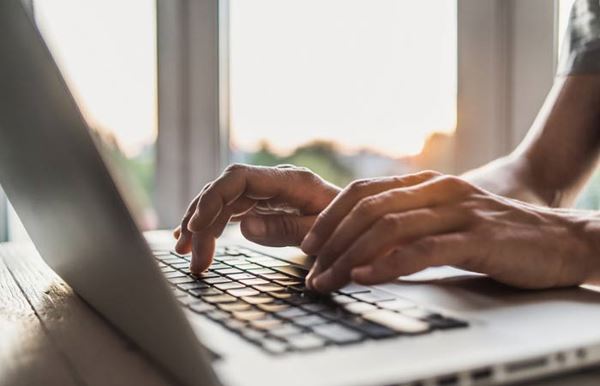 Hands typing on a laptop keyboard as the sun sets.