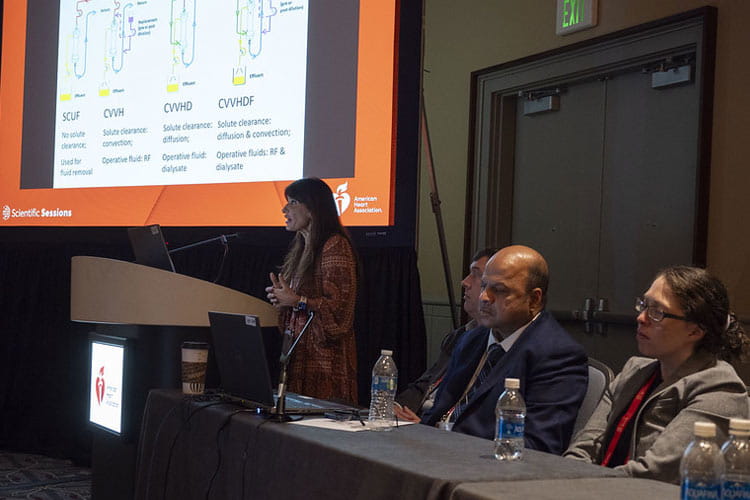 A presenter speaks to the Heart/Kidney Symposium while moderators look on in 2024.