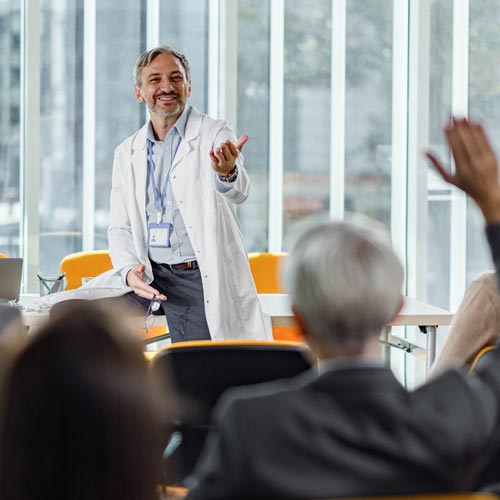 A photo of a man in a doctor's coat answering a question from his presentation audience.