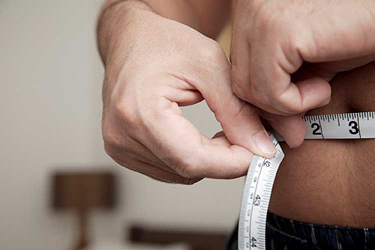 A closeup image of a man measuring his waist with a measuring tape.